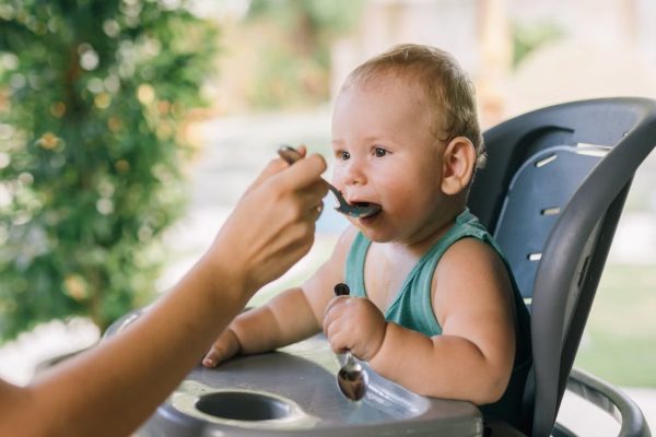 Cute baby eating with a spoon in a high chair outdoors. Calm and precious moment.